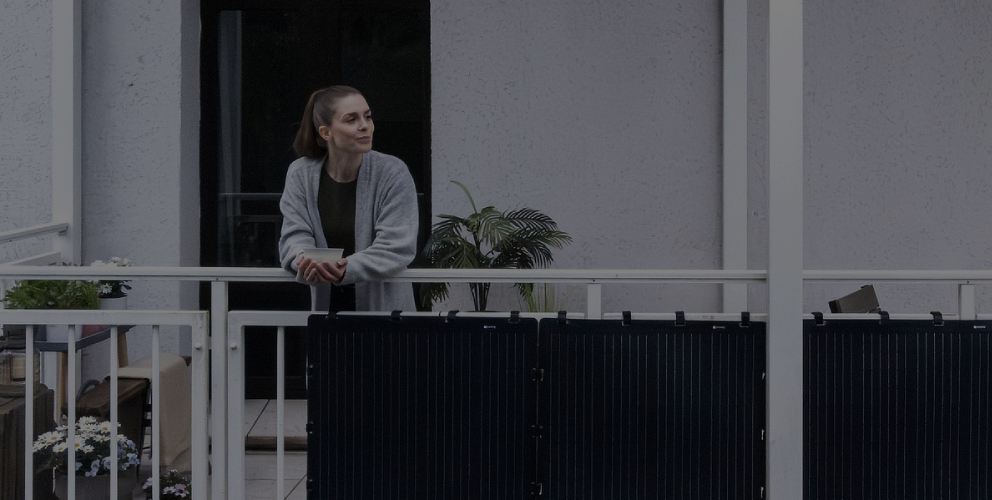 Aktion: 4 % Rabatt für Vattenfall-Kund:innen. Eine Frau lehnt entspannt an einem Balkon, an dem schwarze Solarpaneele befestigt sind.