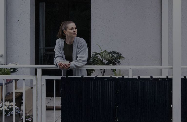 Aktion: 4 % Rabatt für Vattenfall-Kund:innen. Eine Frau lehnt entspannt an einem Balkon, an dem schwarze Solarpaneele befestigt sind.
