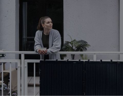 Aktion: 4 % Rabatt für Vattenfall-Kund:innen. Eine Frau lehnt entspannt an einem Balkon, an dem schwarze Solarpaneele befestigt sind.