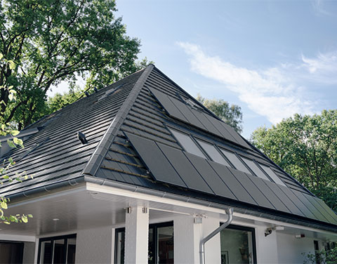 Solarpaneele auf einem Einfamilienhaus umgeben von grünen Bäumen.