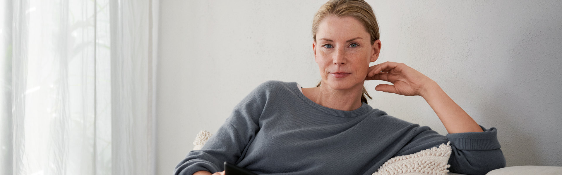 Eine Frau sitzt auf einem Sofa und schaut in die Kamera.