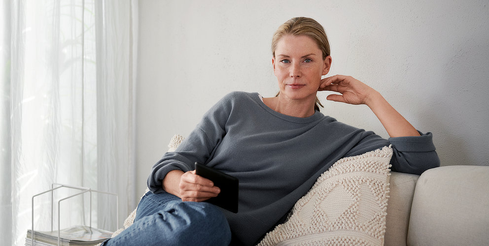 Eine Frau sitzt auf einem Sofa und schaut in die Kamera.