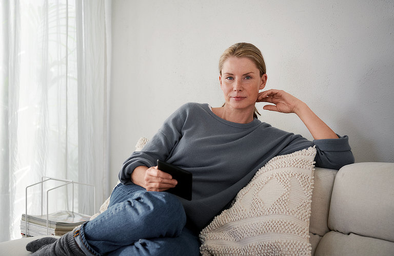 Eine Frau sitzt auf einem Sofa und schaut in die Kamera.