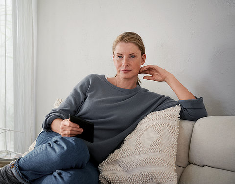 Eine Frau sitzt auf einem Sofa und schaut in die Kamera.