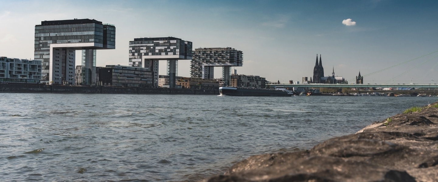 Blick auf die Stadt Köln mit dem Rhein und den Kranhäusern im Vordergrund und dem Kölner Dom im Hintergrund.
