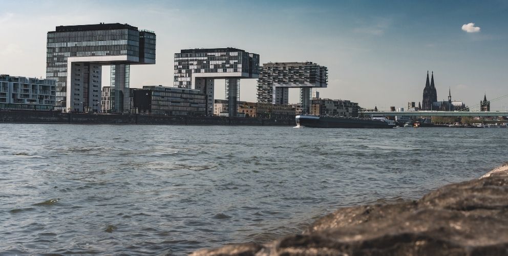 Blick auf die Stadt Köln mit dem Rhein und den Kranhäusern im Vordergrund und dem Kölner Dom im Hintergrund.