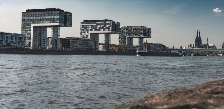 Blick auf die Stadt Köln mit dem Rhein und den Kranhäusern im Vordergrund und dem Kölner Dom im Hintergrund.