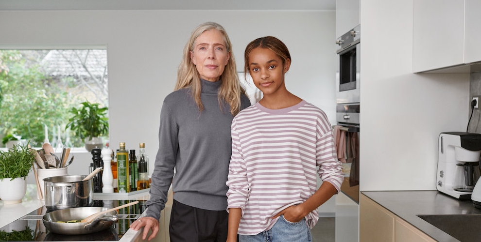 Eine Frau und ein Mädchen stehen eng nebeneinander in einer modernen und hellen Küche. Beide blicken ein wenig lächelnd direkt in die Kamera.