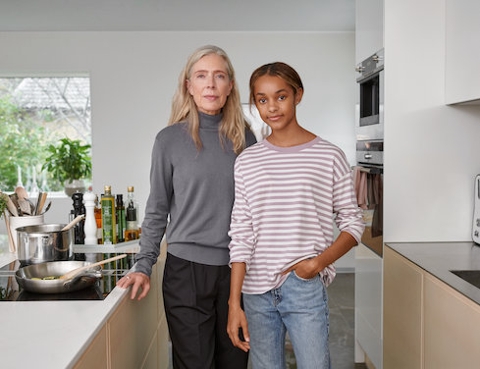 Eine Frau und ein Mädchen stehen eng nebeneinander in einer modernen und hellen Küche. Beide blicken ein wenig lächelnd direkt in die Kamera.