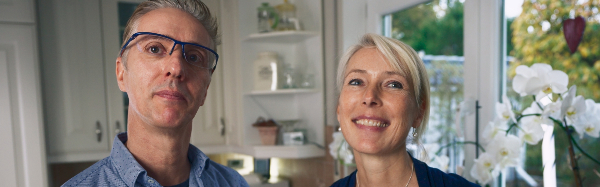 Mann und Frau stehen in einer modernen und hellen Küche. Beide blicken freudig in die Kamera.