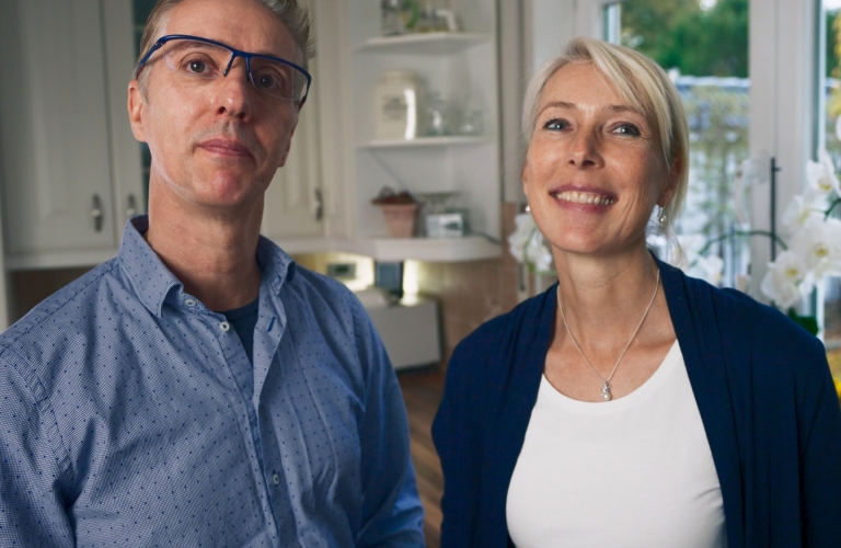 Mann und Frau stehen in einer modernen und hellen Küche. Beide blicken freudig in die Kamera.