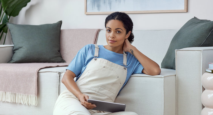 Frau sitzt mit einem Tablet in der Hand vor Sofa